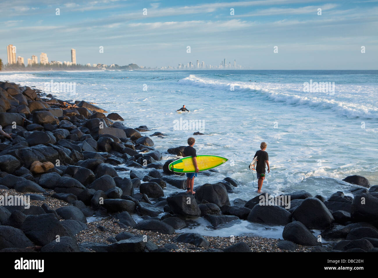 Surfers climbing over rocks to reach surf at Burleigh Heads. Gold Coast