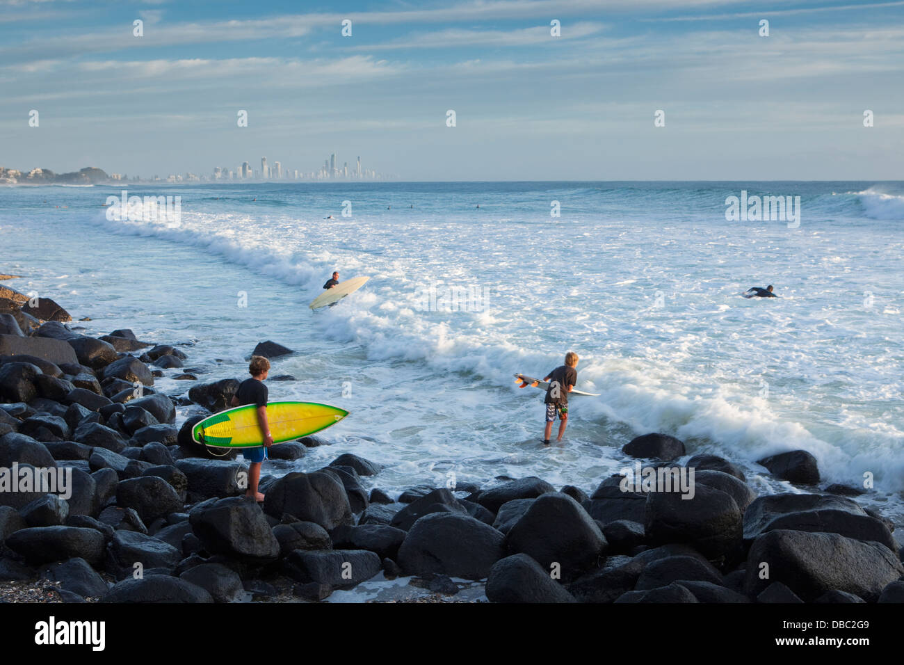 Surfers climbing over rocks to reach surf at Burleigh Heads. Gold Coast