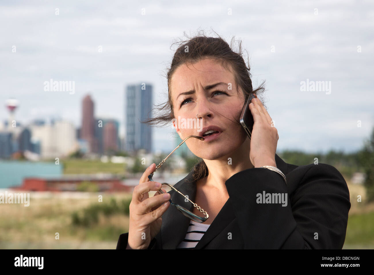 Serious business woman using iPhone outdoors with downtown city skyline in background Stock Photo