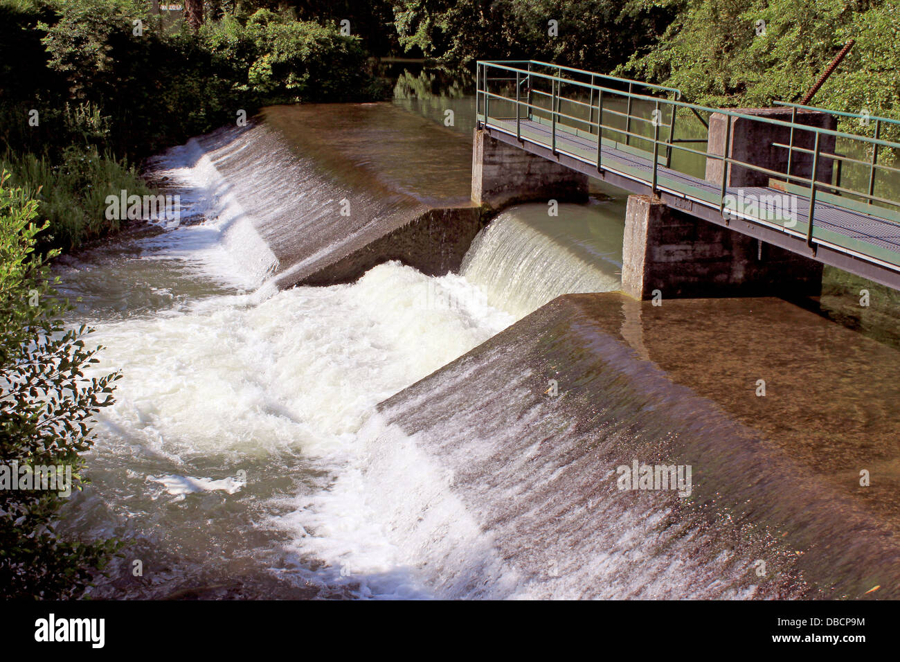 a dam retaining water from a swollen river with its bridge and waterfall Stock Photo