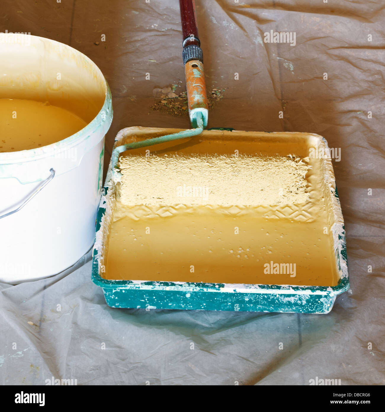 painter roller brush in plastic paint tray with yellow emulsion paint