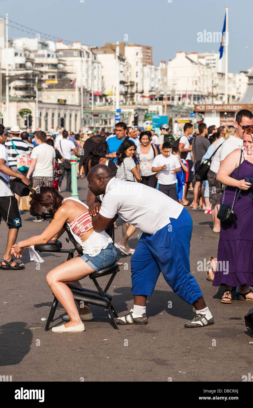 Woman getting a back massage from a masseur, on a busy pavement, Brighton, England, UK. Stock Photo