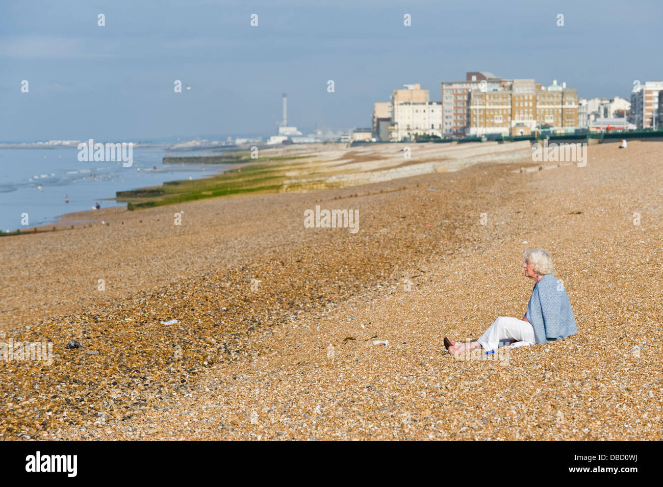 Elderly woman sitting alone on beach in early morning at Brighton East Sussex England UK Stock Photo