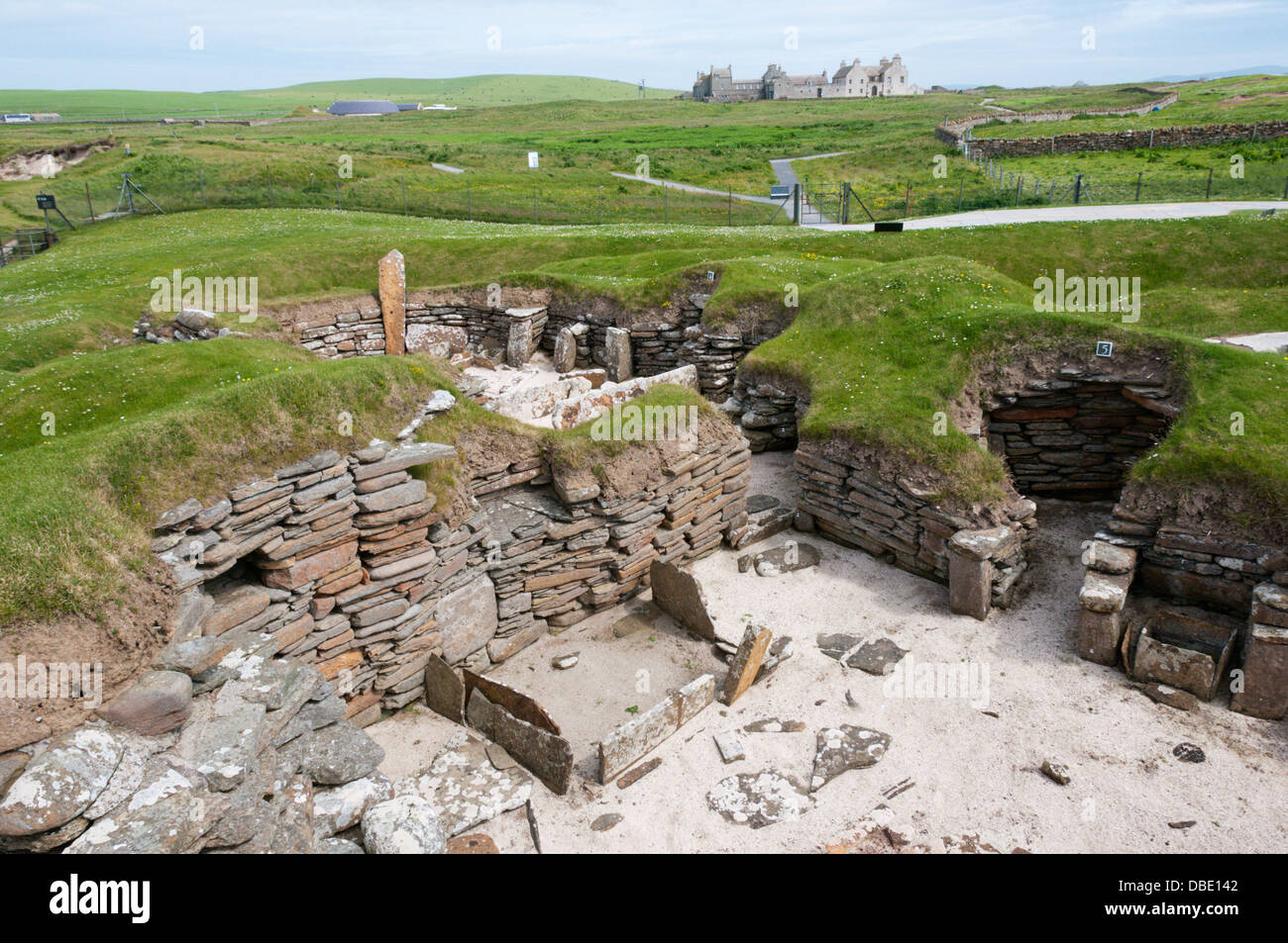 House 5 at Skara Brae Neolithic Village on Mainland Orkney with Skaill House in the background. Stock Photo