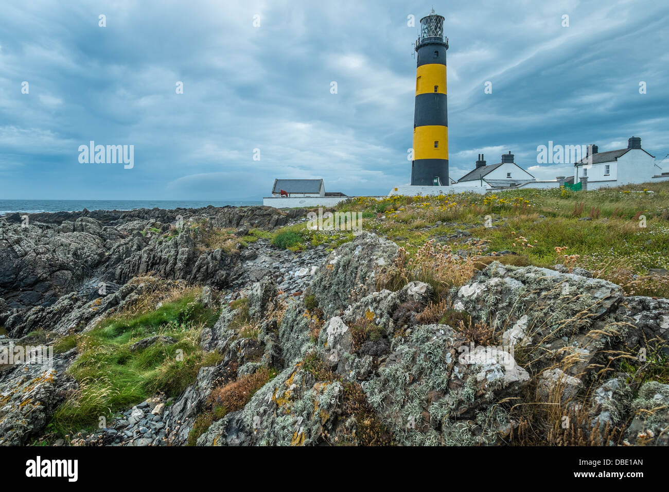 St John's Point Lighthouse in County Down Northern Ireland shown against stormy gray clouds with coastal rock formation in the f Stock Photo