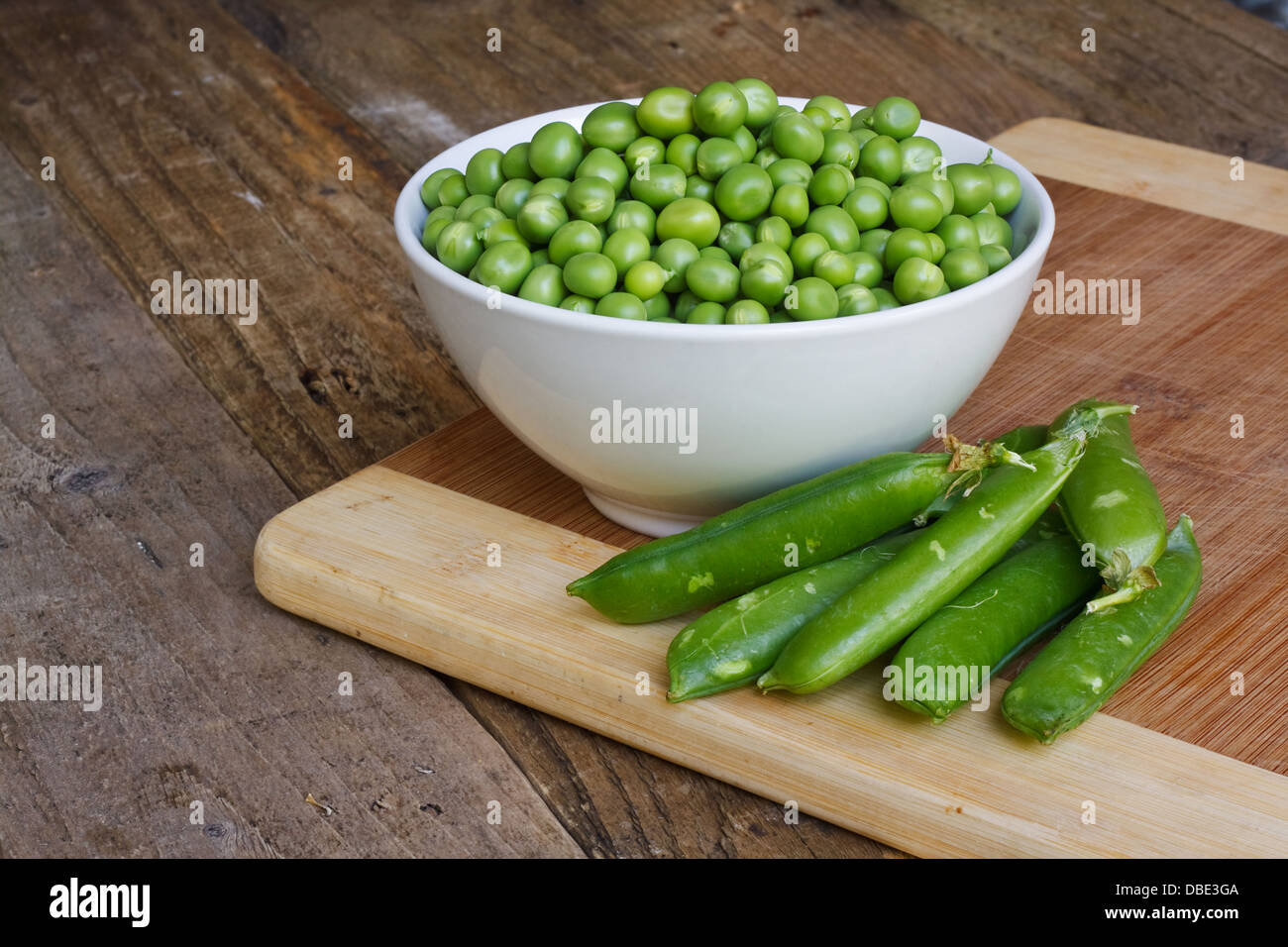 garden peas in a bowl in rustic setting with pea pods Stock Photo
