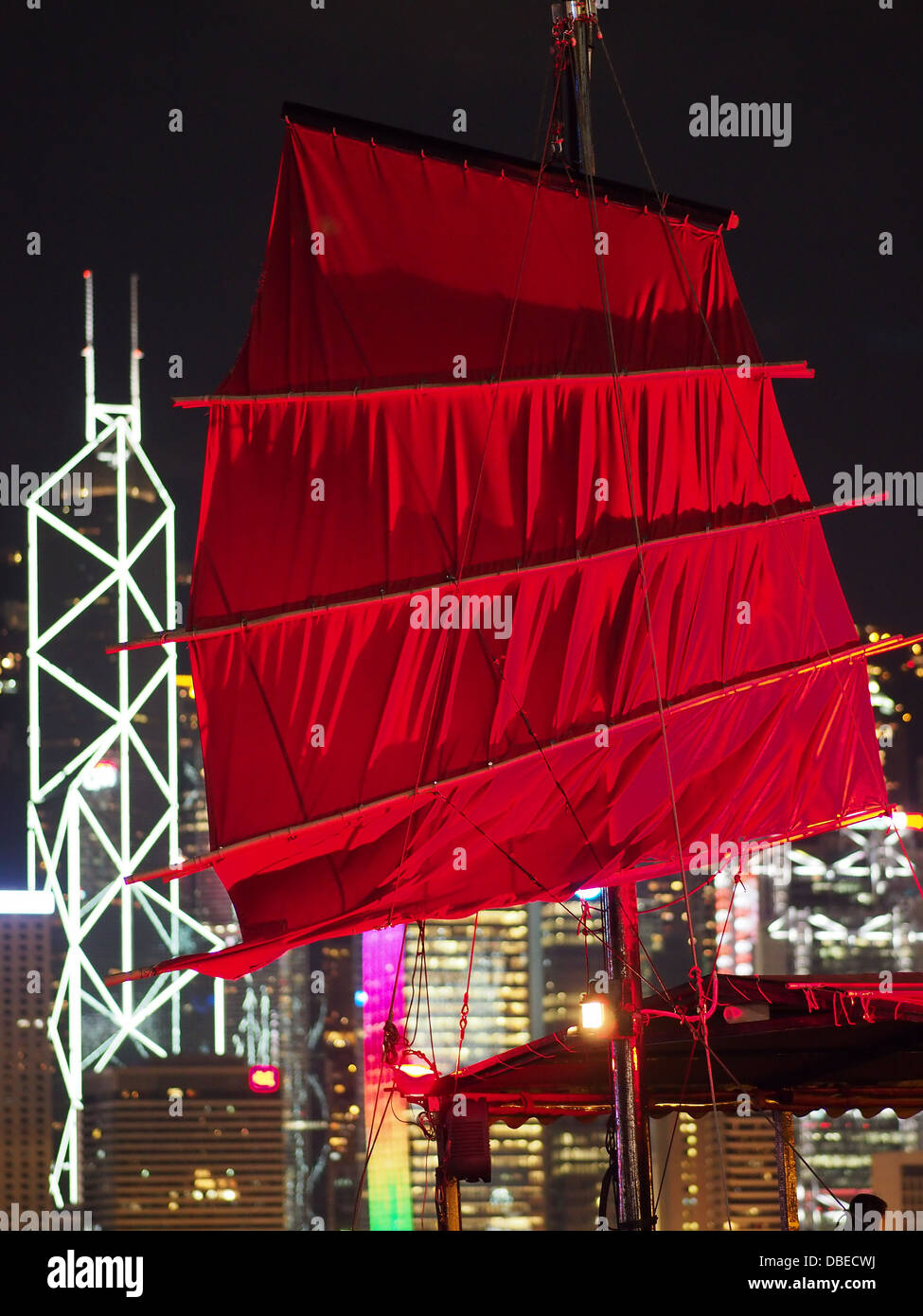 A red sail on a harbour tour Chinese junk at night with Hong Kong in the background Stock Photo