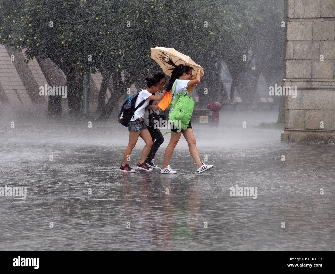 People sheltering from the rain under small umbrella during a tropical downpour in Hong Kong Stock Photo