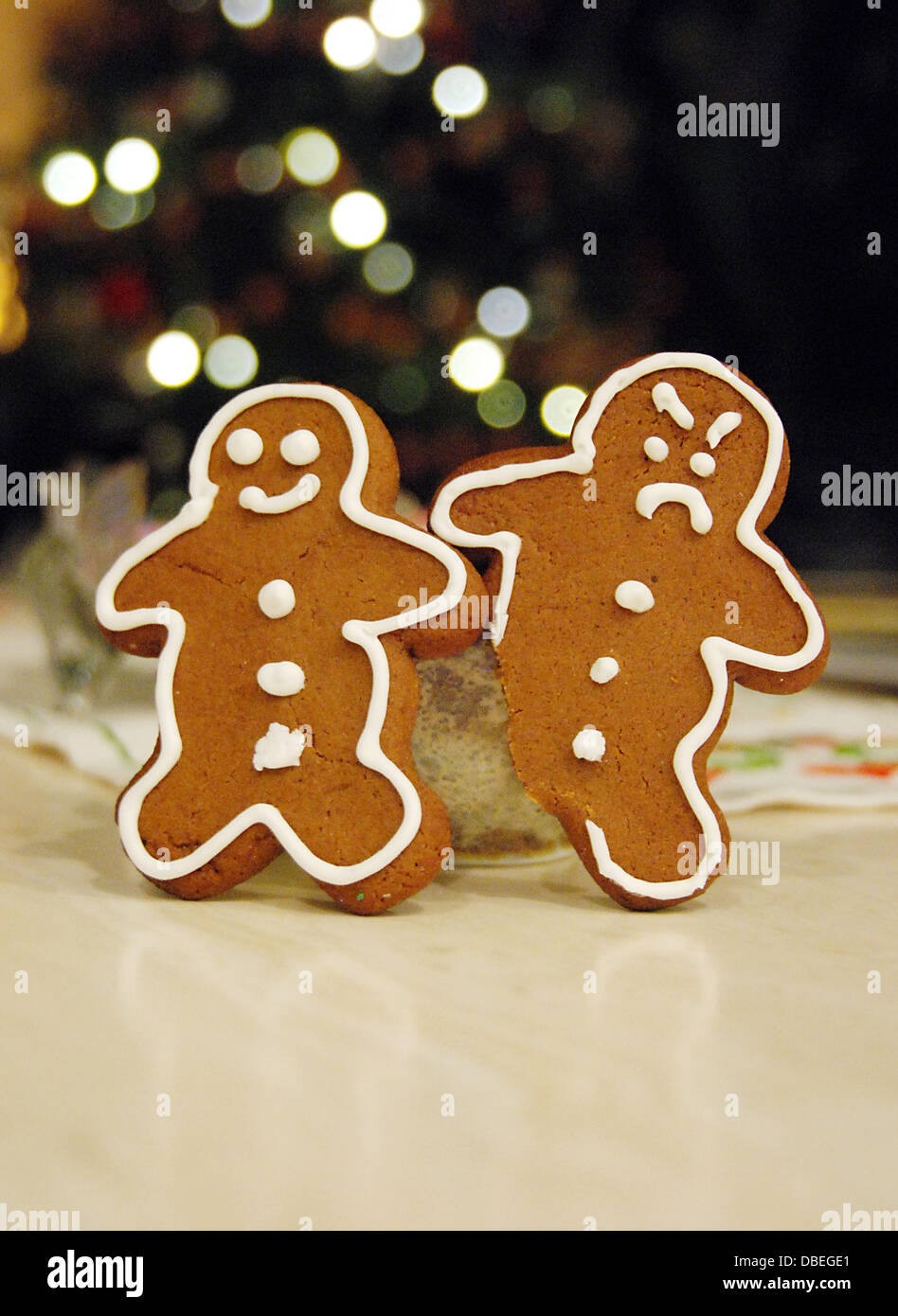 An angry upset grumpy frowning gingerbread man looks at a happy gingerbread man because his leg foot has been bitten Stock Photo