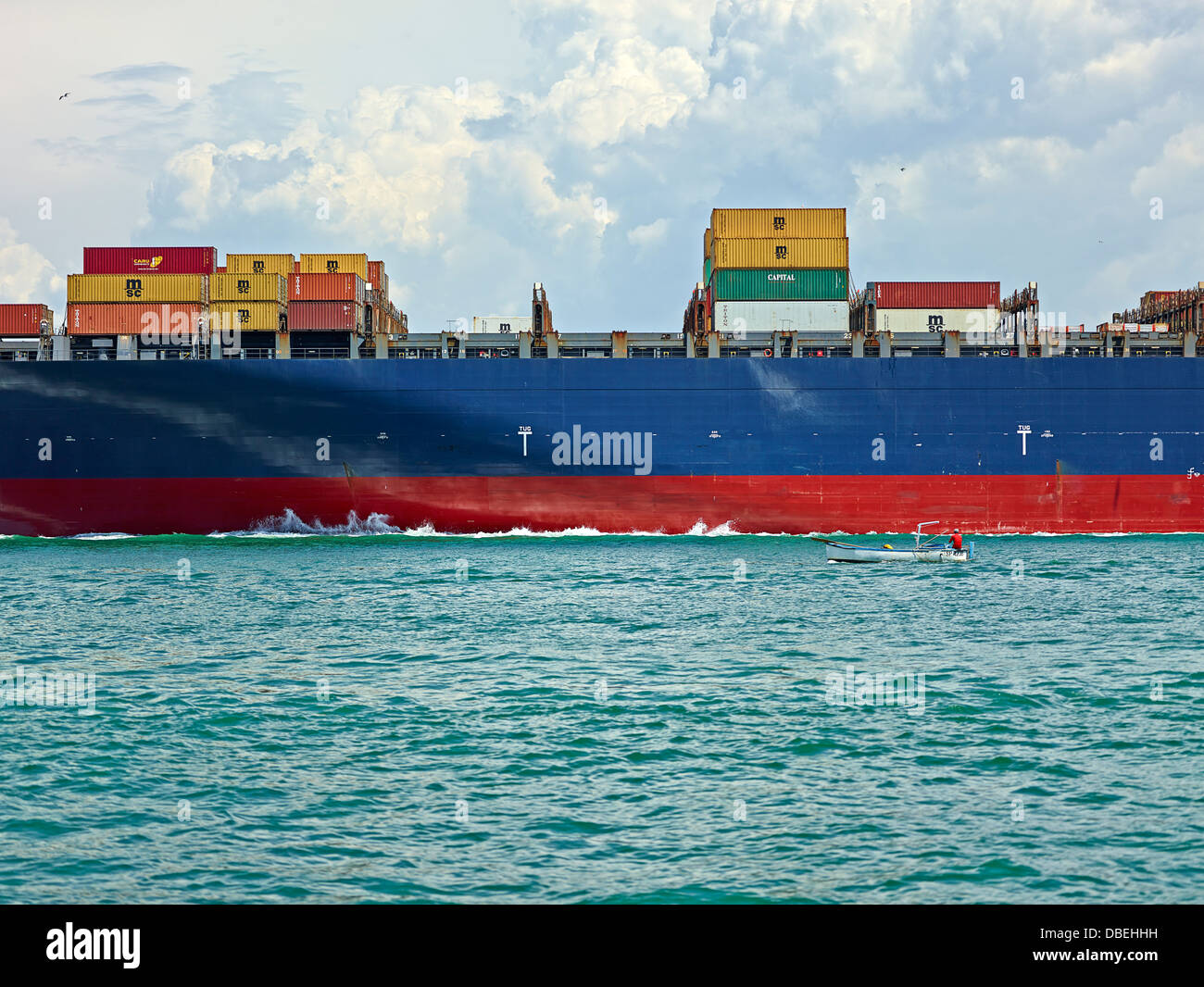 A small motorboat raft next to a large container ship sailing in the ...
