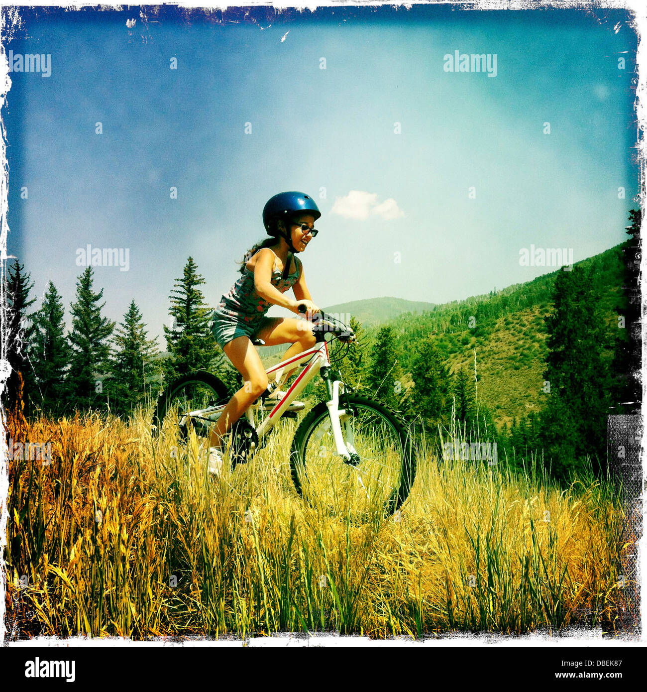 Hispanic girl riding mountain bike in tall grass Stock Photo
