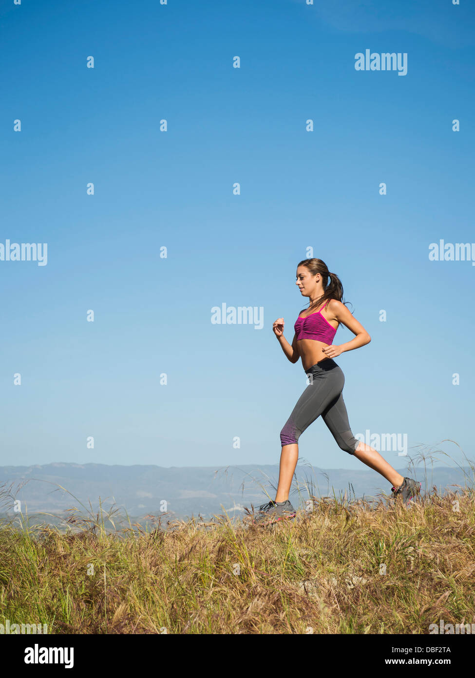 Mixed race woman running in rural landscape Stock Photo