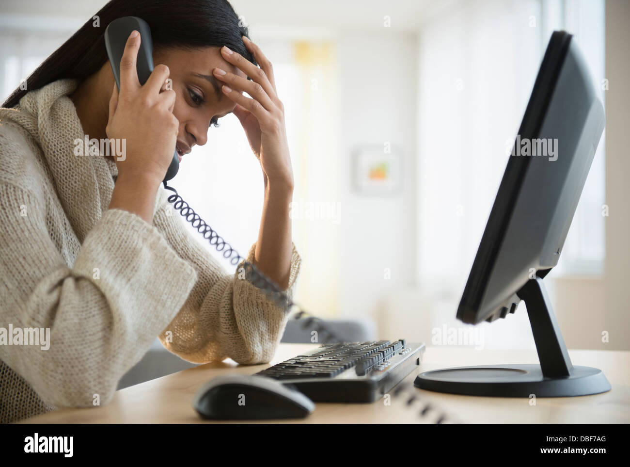 Mixed race woman talking on phone at desk Stock Photo