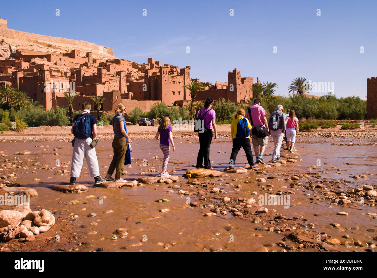 Aït Benhaddou in Berber Ath Benhadu Morocco. Tourists cross the Ounila River . Most of the town's inhabitants now live in a more modern village at the other side of the river; however, eight families still live within the ksar. Stock Photo