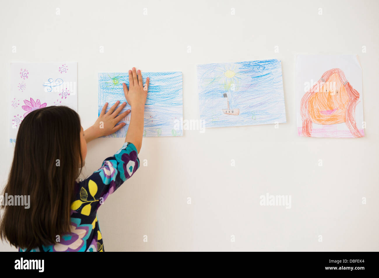 Mixed race girl hanging drawings on wall Stock Photo