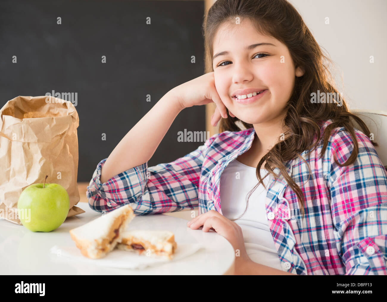 Hispanic girl eating lunch at desk Stock Photo