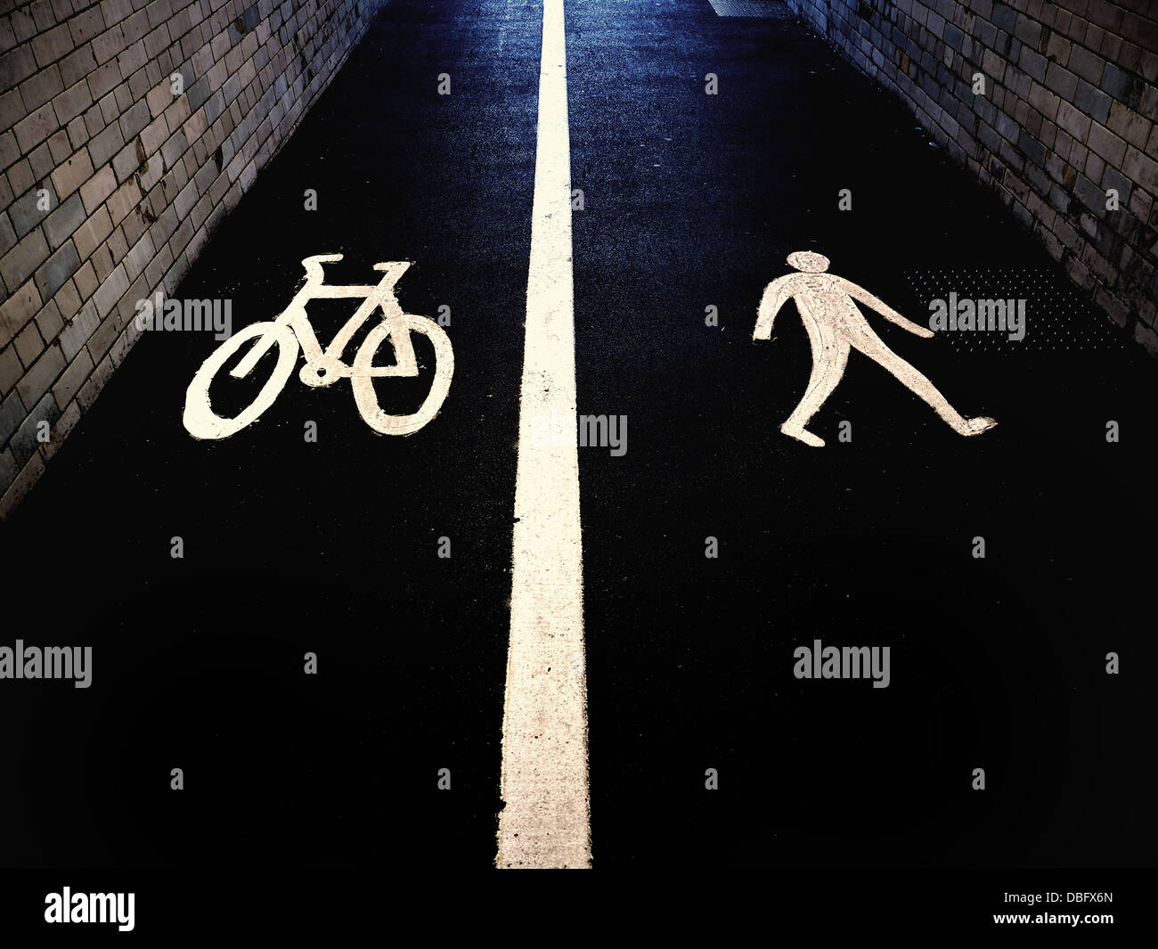 Cycle path and pedestrian symbols on a British sidewalk pavement in a tunnel flanked by brick walls. Stock Photo