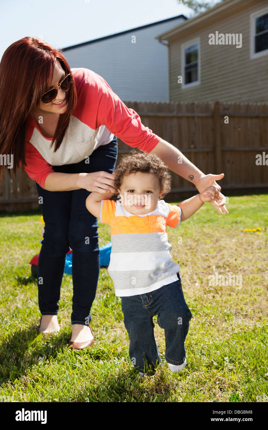Mother helping baby walk in backyard Stock Photo