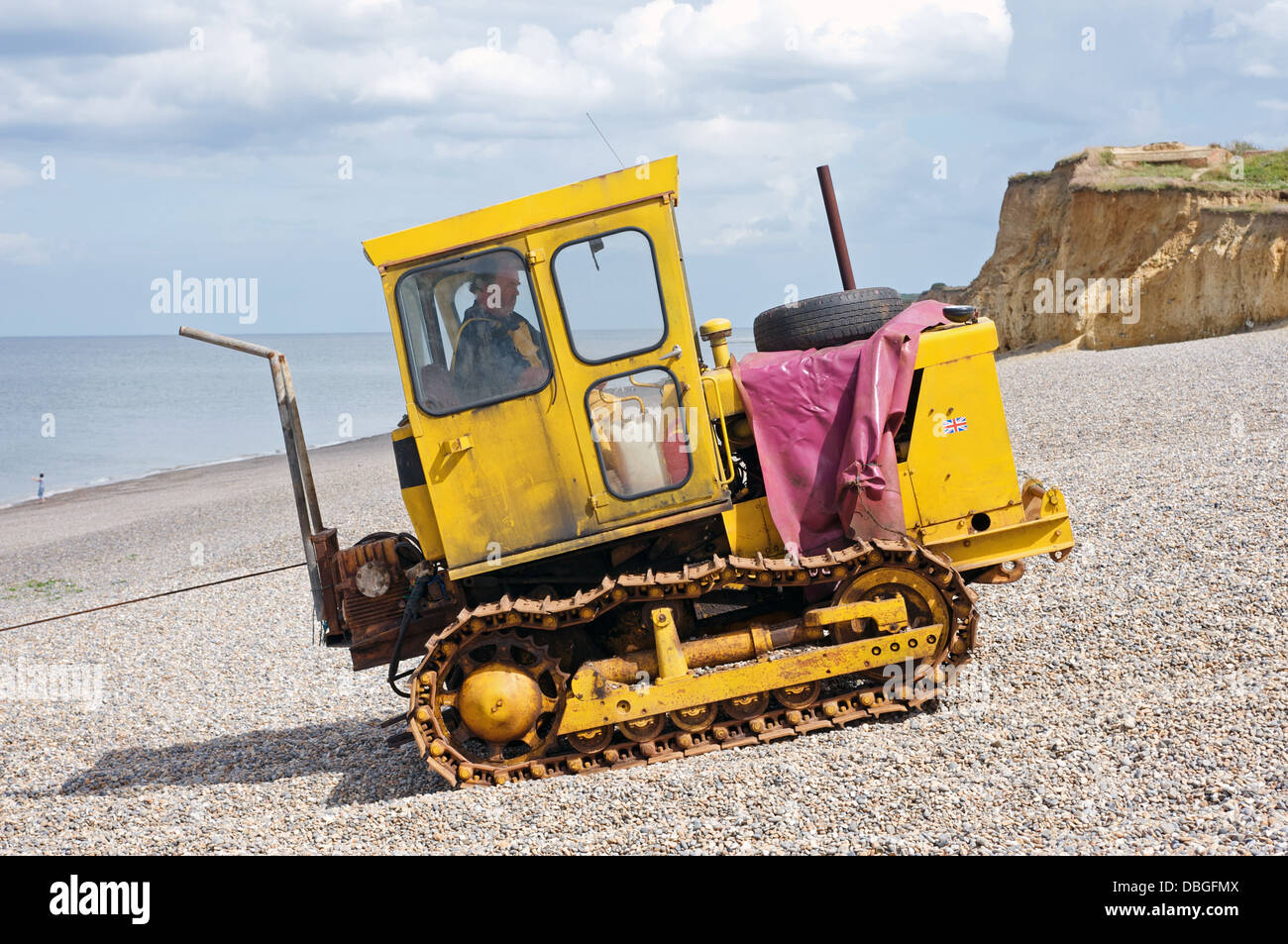 Fisherman operating a caterpillar tractor to pull his fishing boat up the beach, Weybourne, Norfolk, UK. Stock Photo