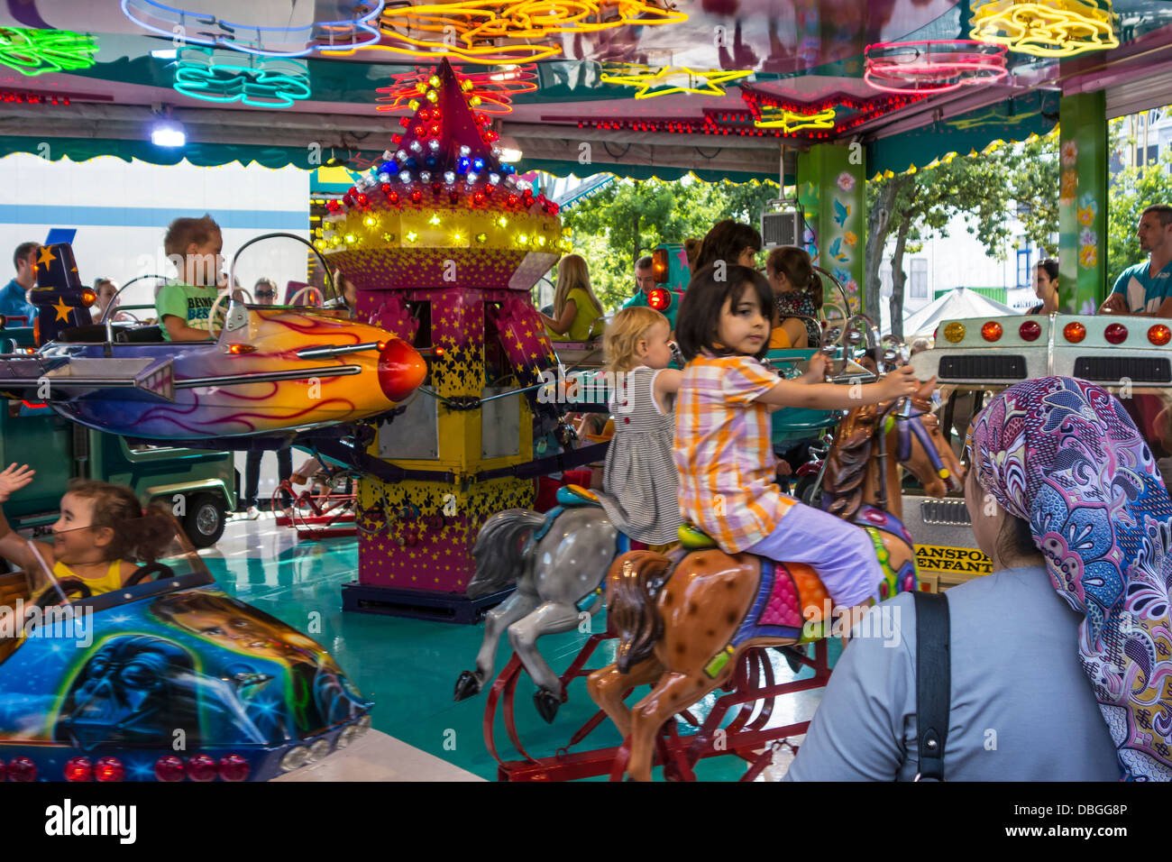 Children riding merry-go-round / carousel at traveling funfair / travelling fun fair Stock Photo