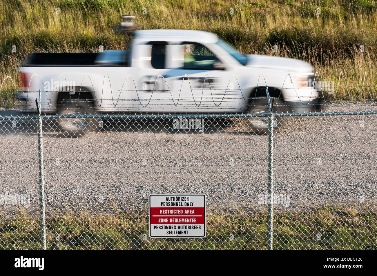 Airport perimeter security: tall fence,razor wire,warning sign and a visual check by airport personnel driving a truck Stock Photo