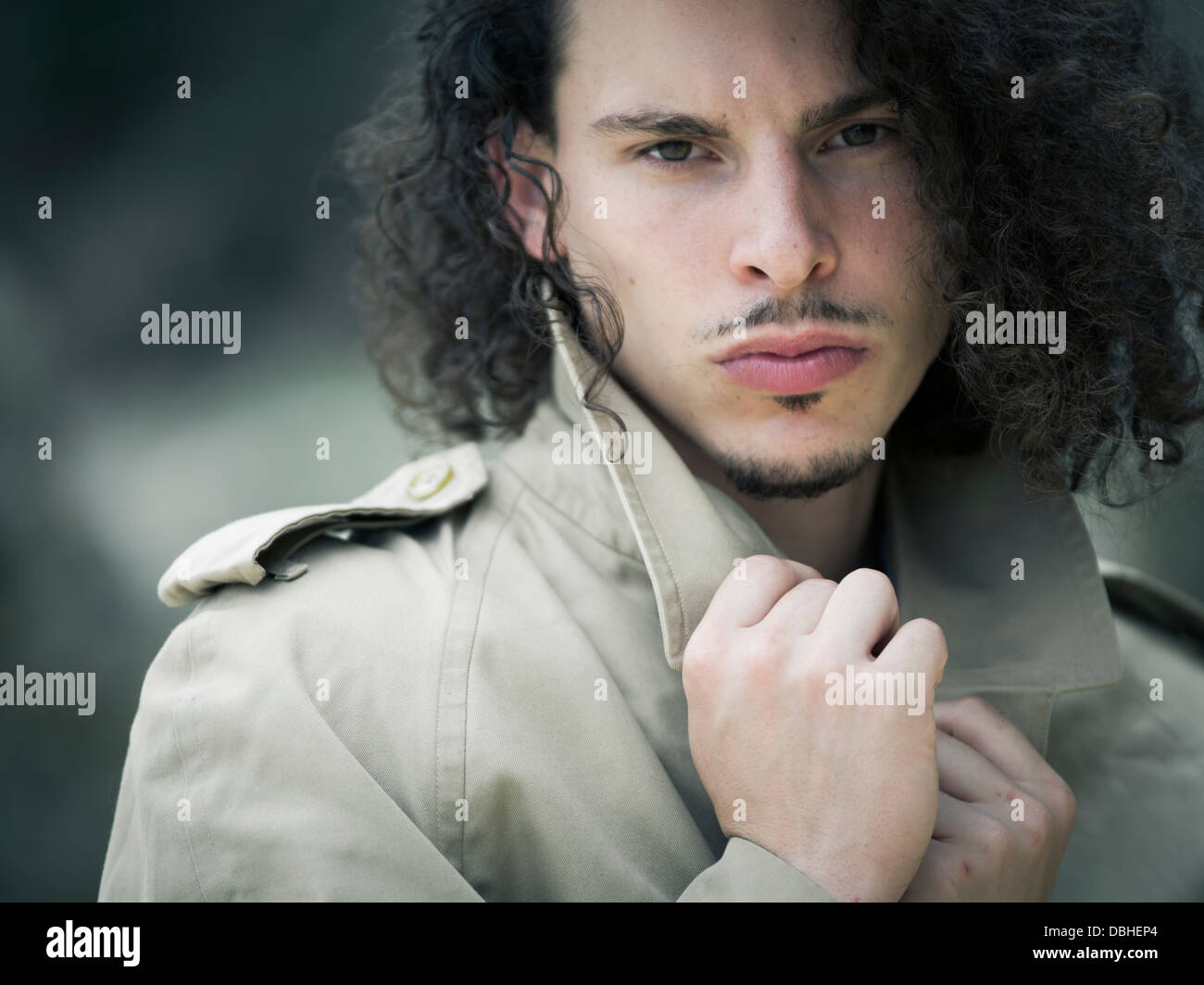 Man with long wavy hair beard and mustache wearing Burberry trench coat  raincoat Stock Photo