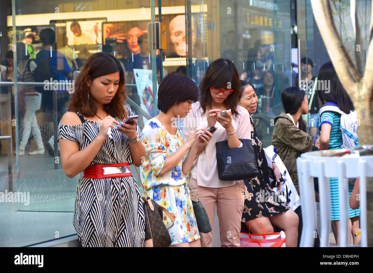 Three Asian women using iPhone smartphones outside the Apple Retail Store in Causeway Bay, Hong Kong. Stock Photo