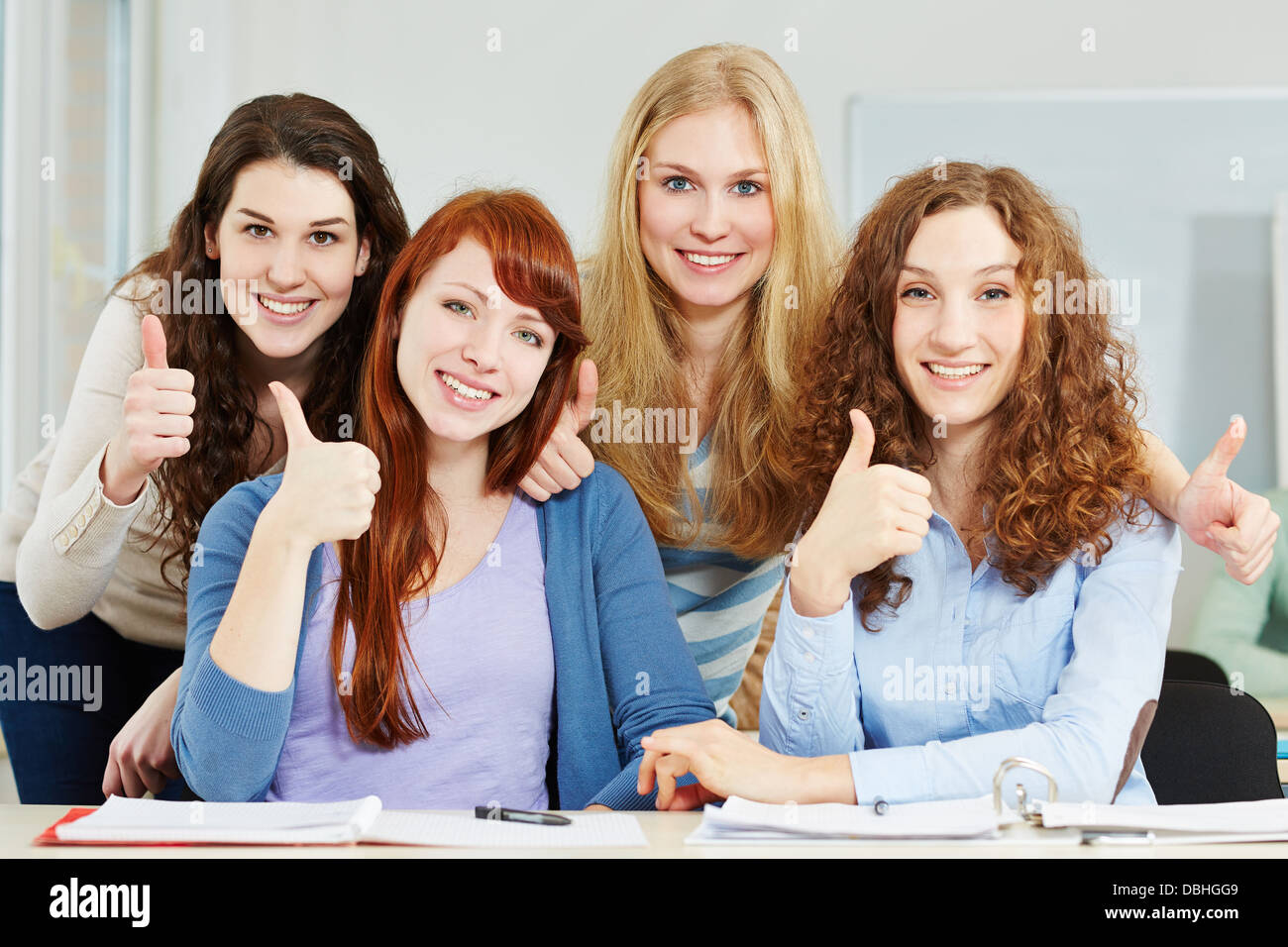 Four attractive happy women holding their thumbs up in university Stock Photo