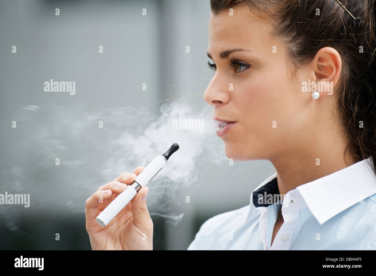 young female smoker smoking e-cigarette outdoors. Head and shoulders, side view Stock Photo
