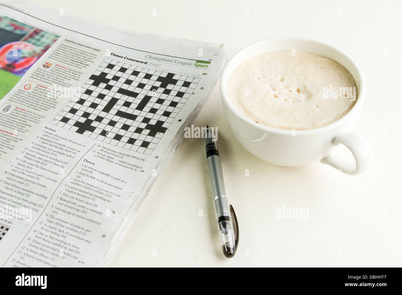The Times newspaper open at the cryptic crossword page with a pen and a cup of cappuccino coffee beside it. Stock Photo