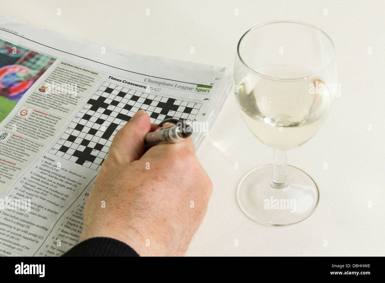 The Times newspaper open at the cryptic crossword page with a man's hand holding a pen and a glass of white wine beside it. Stock Photo