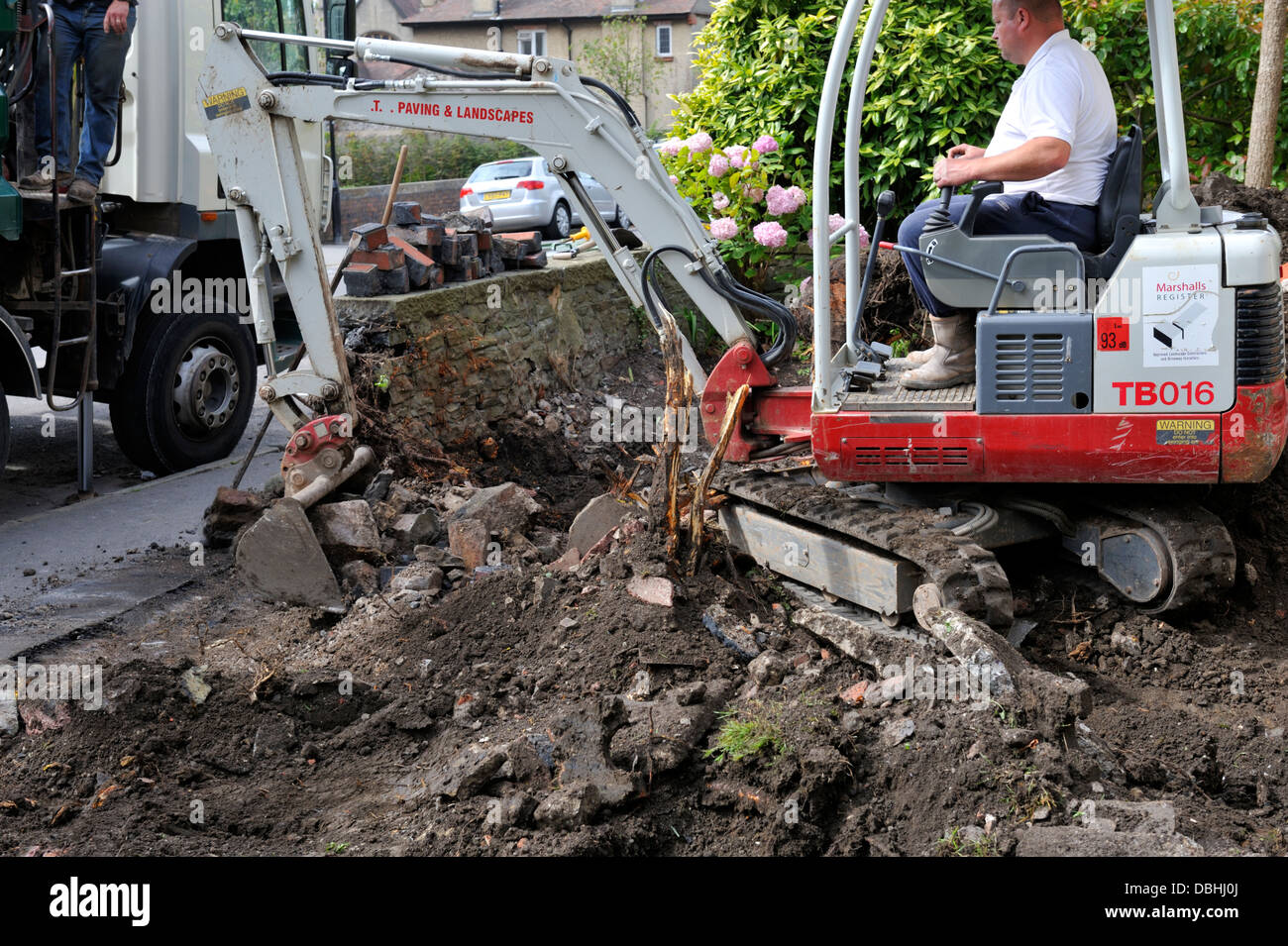 Mini digger working in domestic garden removing stone wall and soil Stock Photo