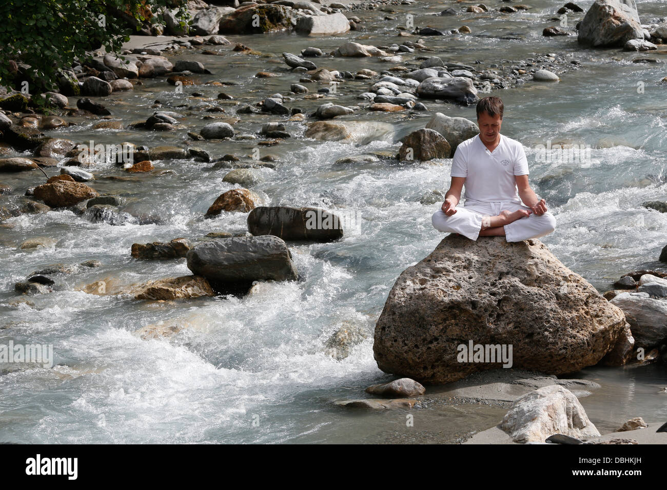Man meditating in the lotus position, sitting on a rock by the river. Stock Photo