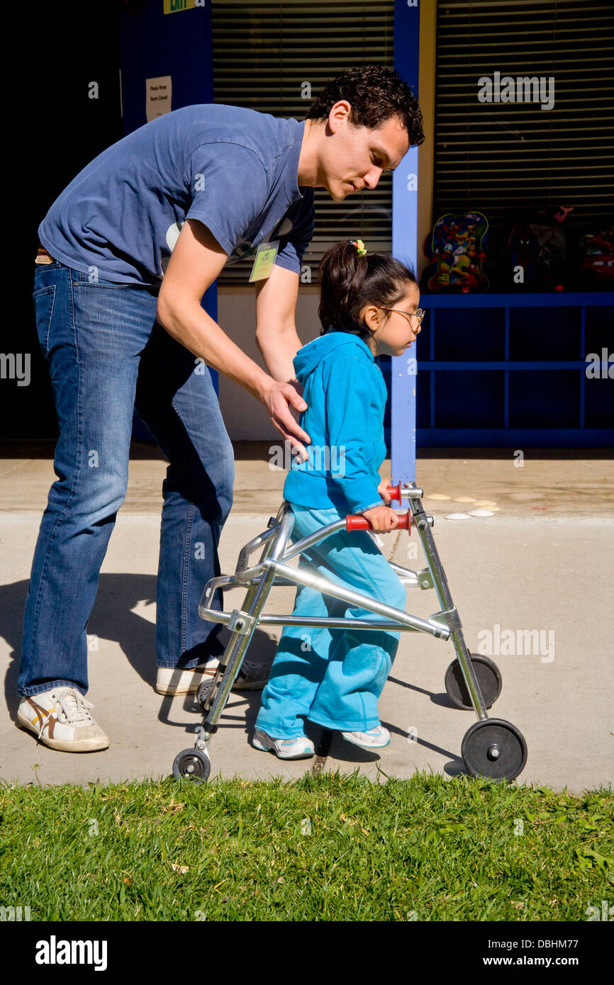 A male staff member helps a blind and crippled Asian American child walk using a special walker Stock Photo