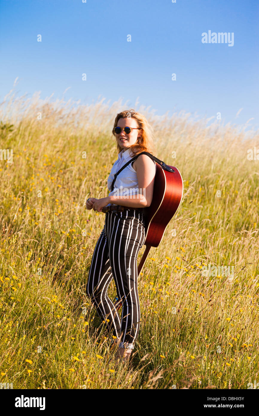 Teenage girl walking through a grassy field carrying a guitar. Outdoors. Summer. Stock Photo