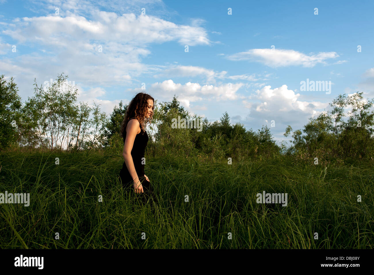 Beautiful girl walks and dreams in high grass on the banks of river ...