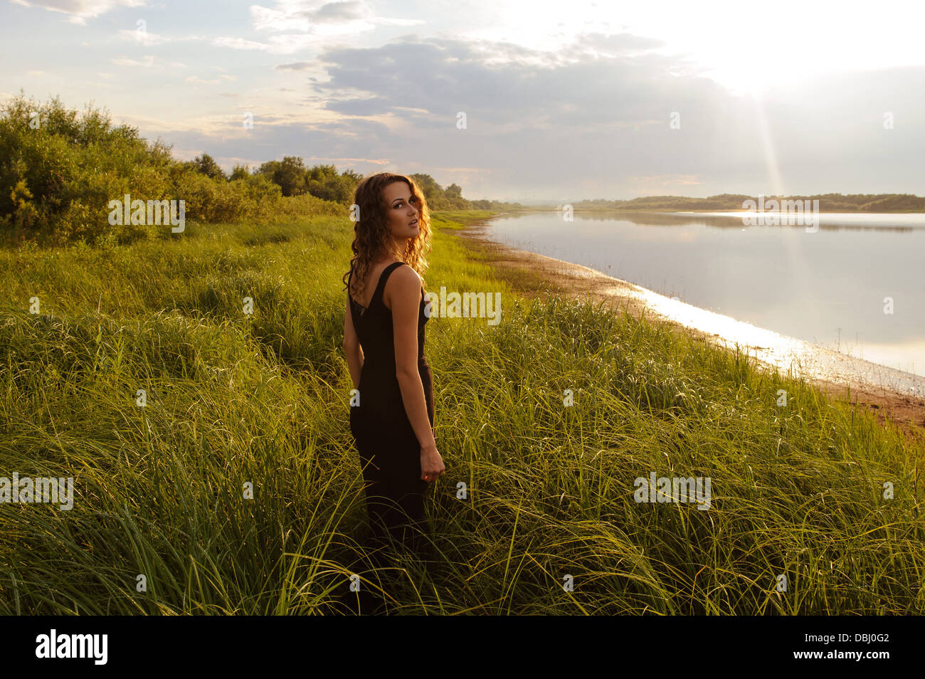 Beautiful girl walks and dreams in high grass on the banks of river ...