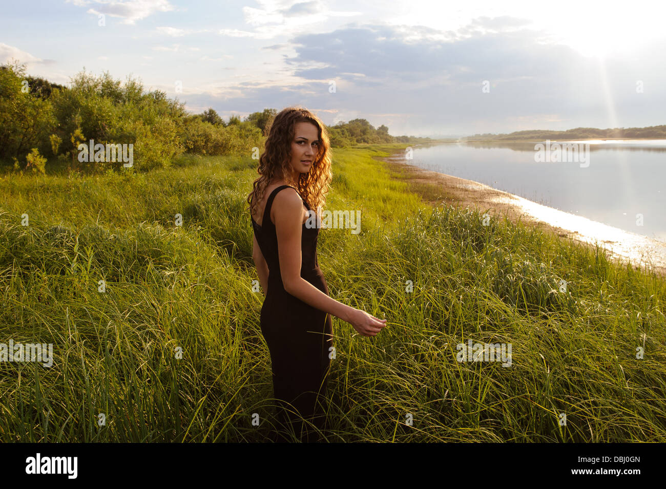 Beautiful girl walks and dreams in high grass on the banks of river ...