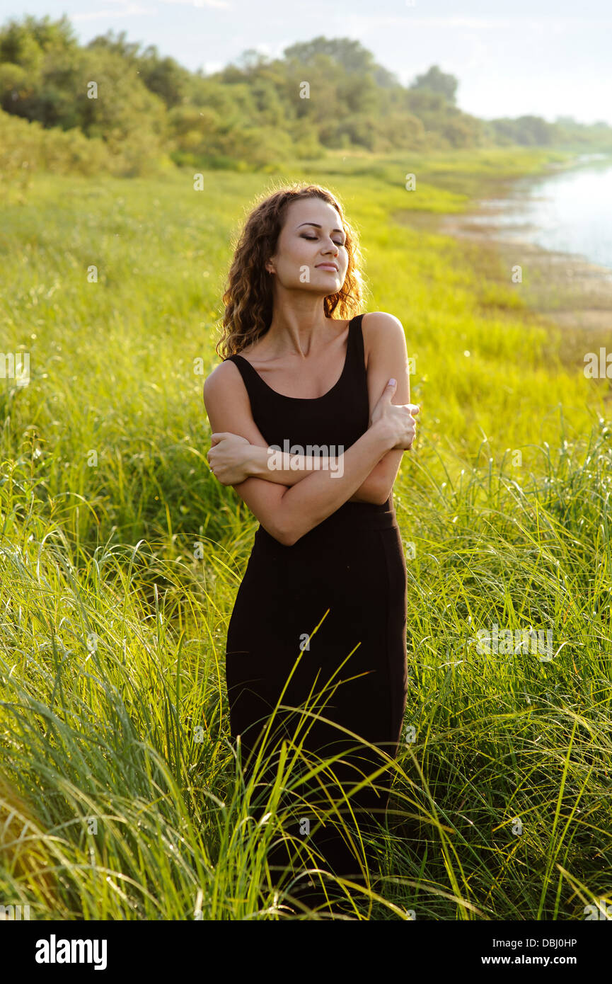 Beautiful girl walks and dreams in high grass on the banks of river ...