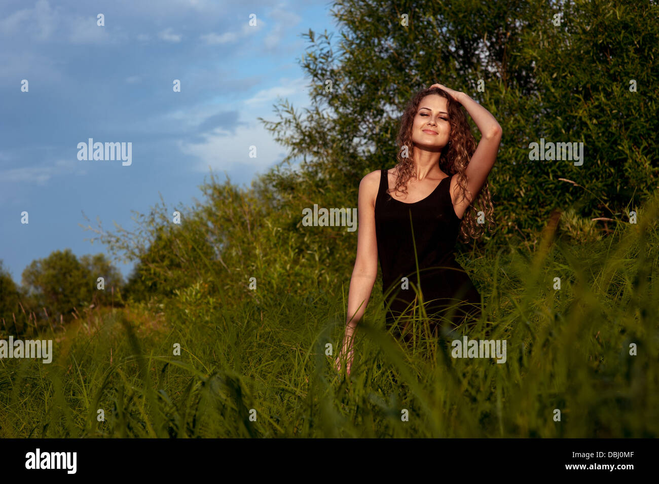Beautiful girl walks and dreams in high grass on the banks of river ...