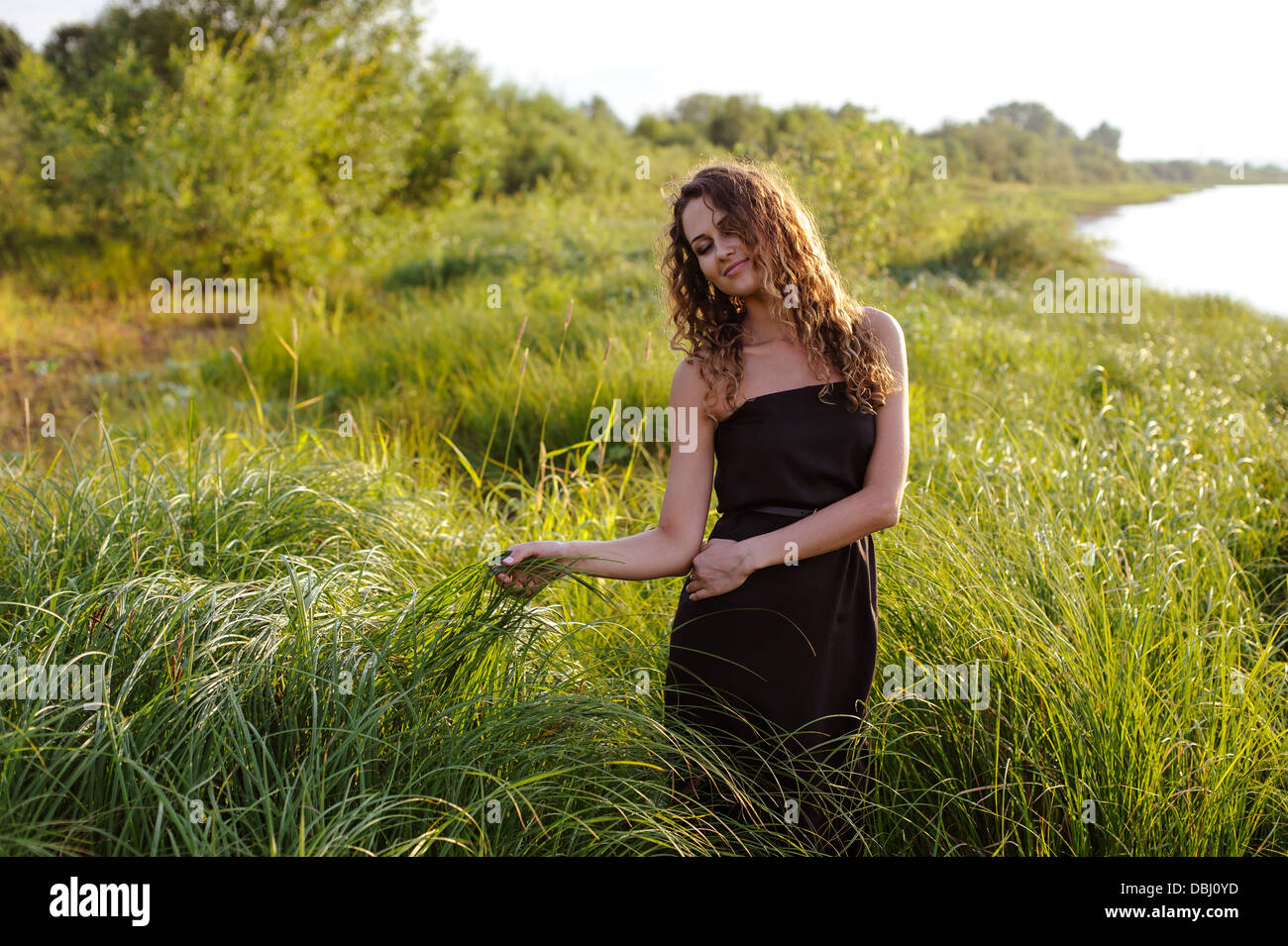 Beautiful girl walks and dreams in high grass on the banks of river ...