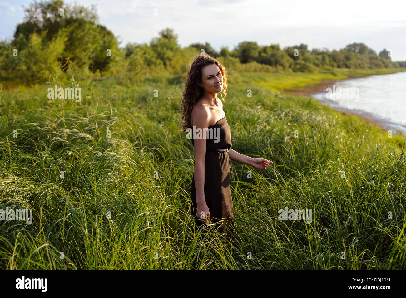 Beautiful girl walks in high grass on the banks of river. Stock Photo