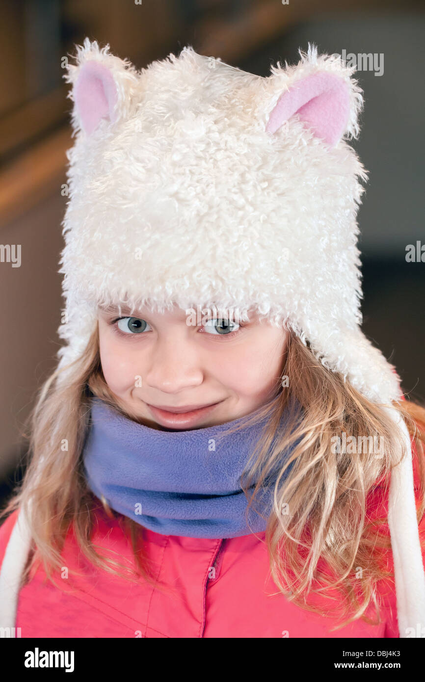 Little blond girl in fun white artificial fur hat. Closeup outdoor portrait Stock Photo