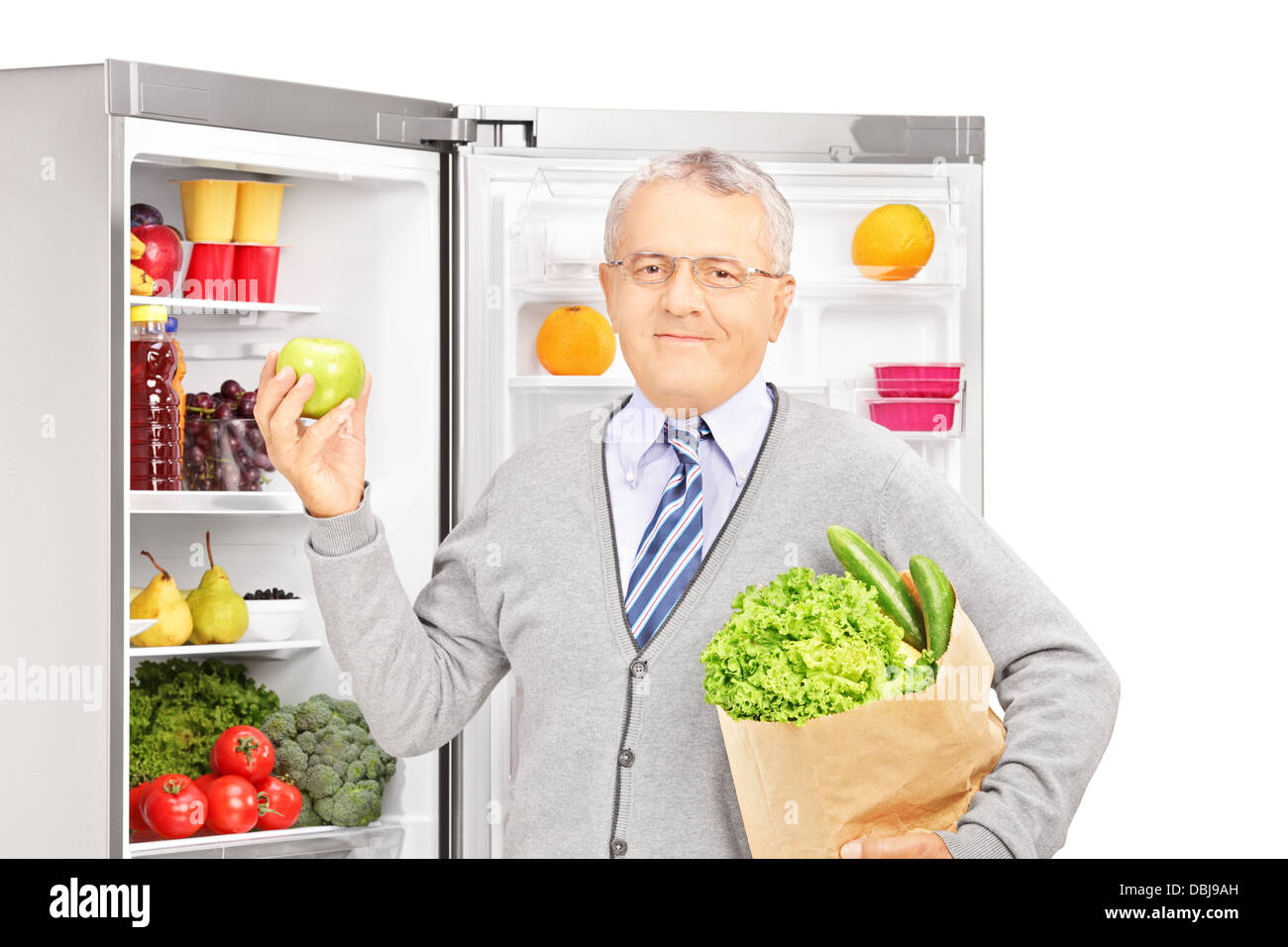 Smiling mature man holding a paper bag next to a refrigerator full of products Stock Photo