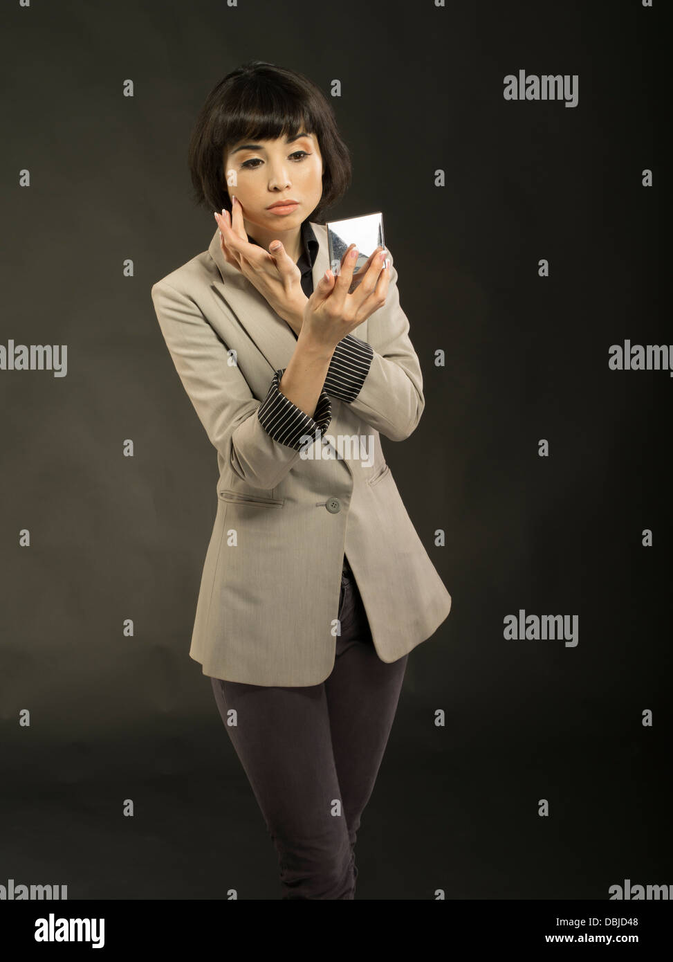 Young beautiful woman in her twenties checking makeup in mirror inside compact Stock Photo