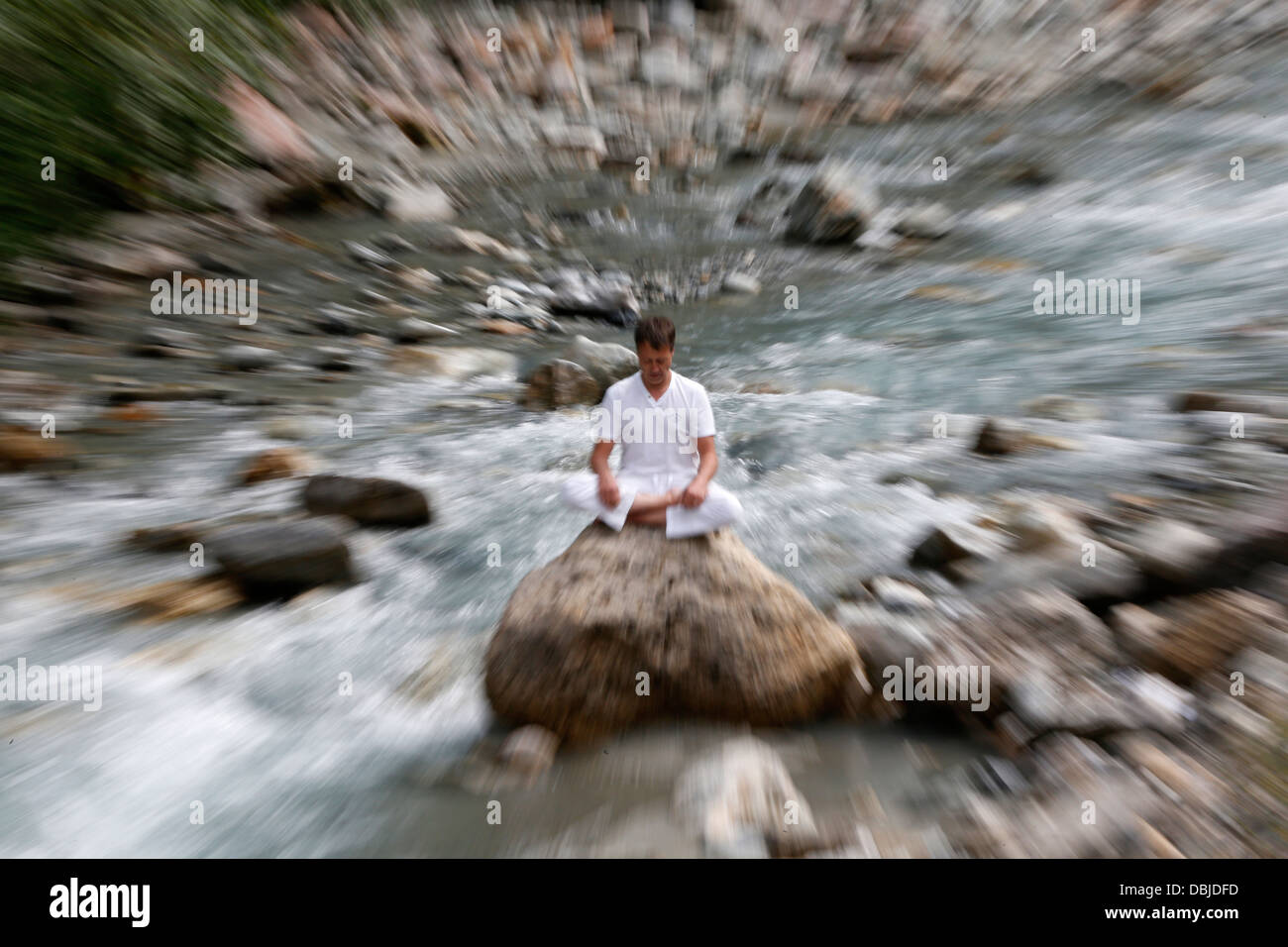 Man meditating in the lotus position, sitting on a rock by the river. Stock Photo