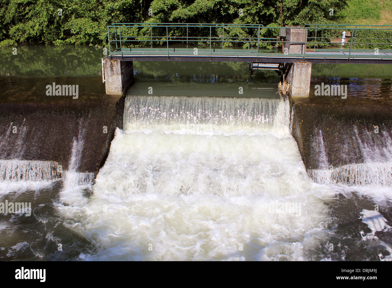 a dam retaining water from a swollen river with its bridge and waterfall Stock Photo