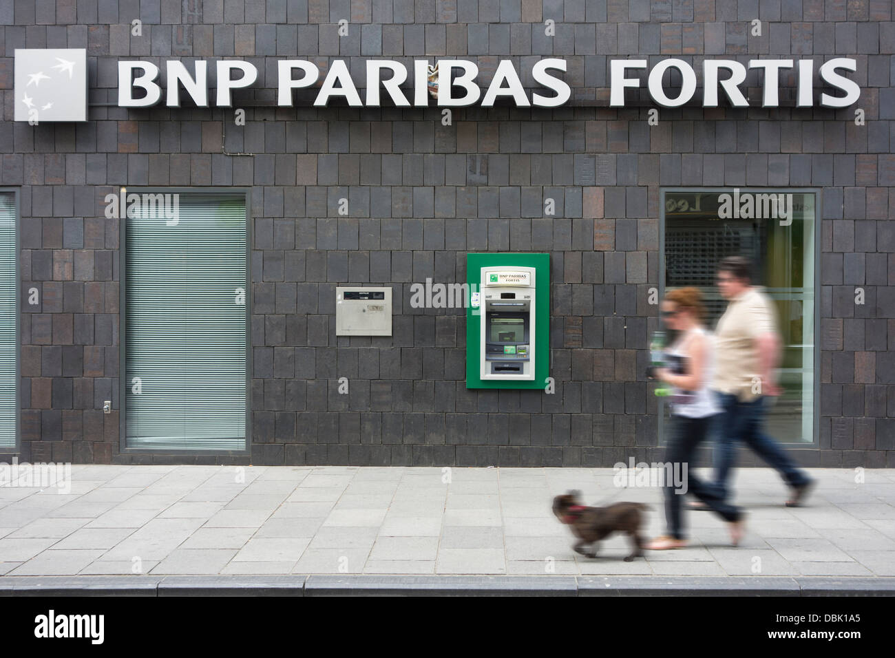 Couple walking past ATM cash dispenser at cashpoint of the BNP Paribas Fortis bank Stock Photo