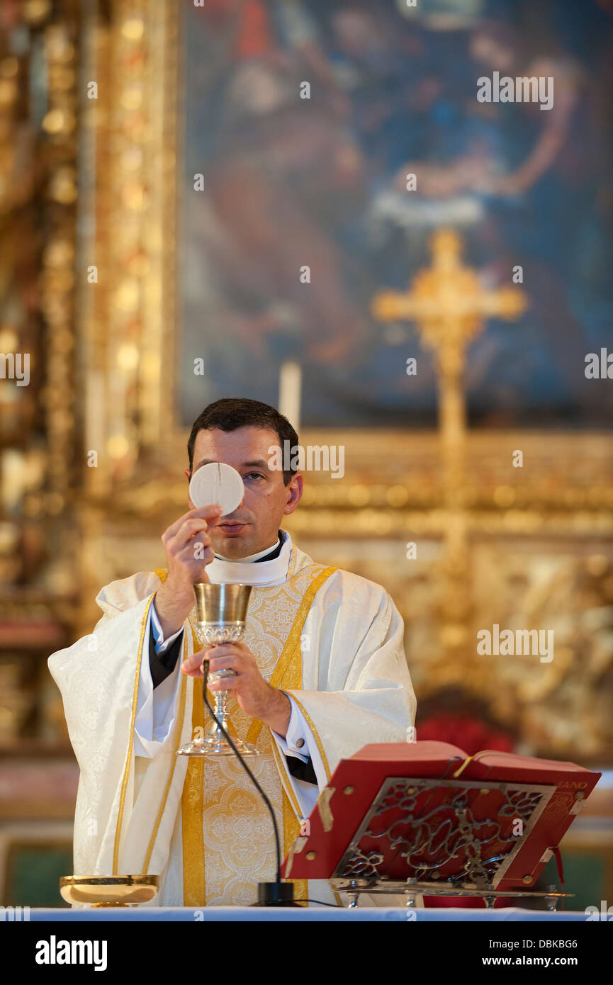 Priest holding host and wine chalice during holy communion while celebrating catholic mass Stock Photo
