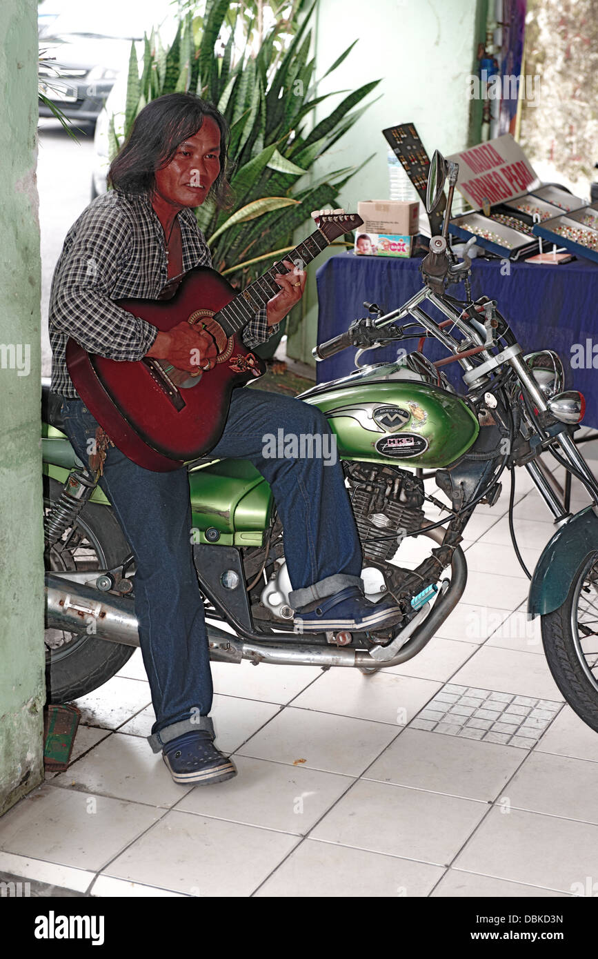Asian man Malay playing guitar on a motorcycle motorbike, Kuchking